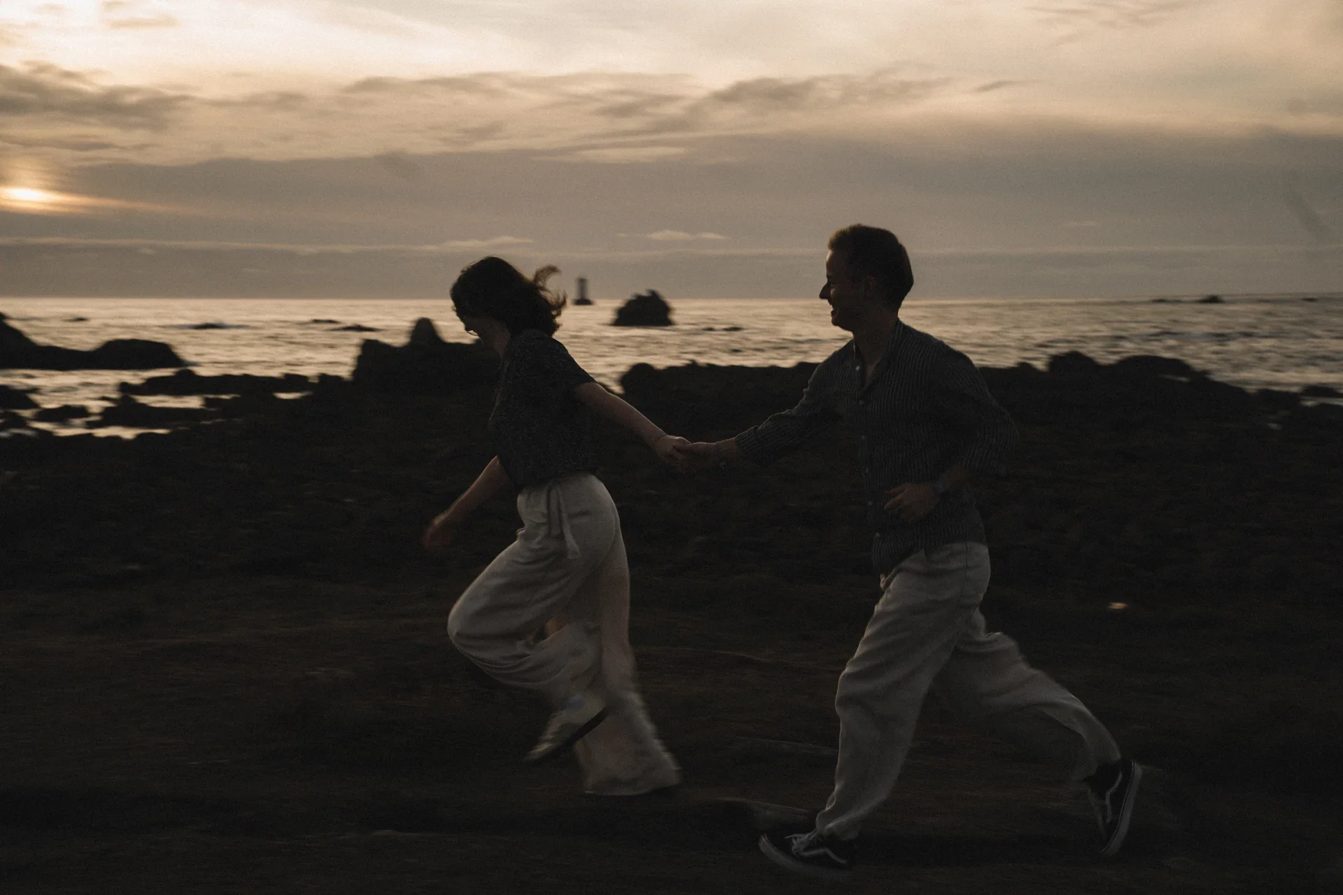 Un couple court main dans la main sur la côte au coucher du soleil