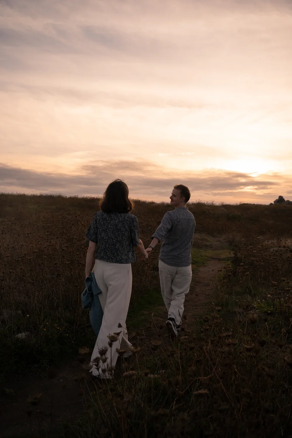 Un couple se promène main dans la main au coucher du soleil